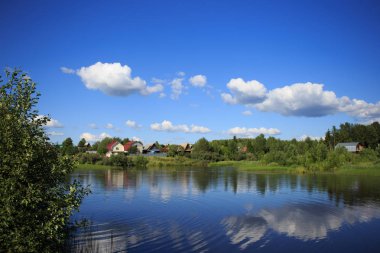 Bulutlu gökyüzü ile küçük bir köy sağtarafı yansıtan Gölü