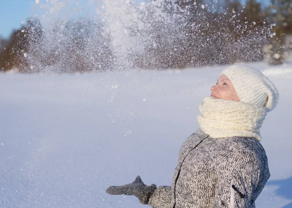 Όμορφη γυναίκα με πλεκτό καπέλο και κασκόλ ρίχνει χιόνι σε ηλιόλουστη χειμωνιάτικη ημέρα — Φωτογραφία Αρχείου