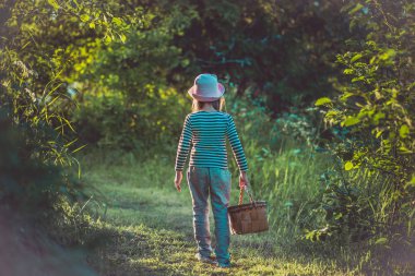 Yeşil ormanda bir sepet taşıyan bir yolda yürüyen genç kız