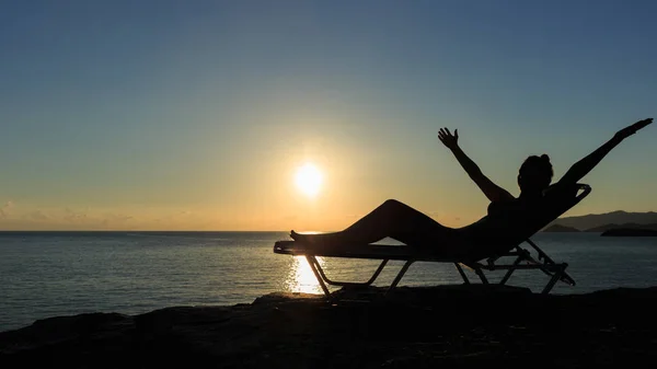 若い女性のシルエットが夕日で、デッキチェアに横たわっています。 — ストック写真