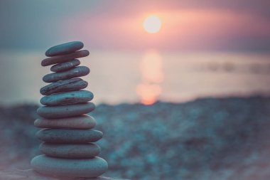 Kum üzerindeki taş piramit zen, ahenk ve dengeyi sembolize eder. Arka planda gün batımında okyanus