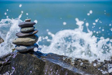 Çakıl taşları piramidini çakıl taşı sahilinde su sıçratan bir dalgayla dengele. İstikrar, denge ve uyum kavramı