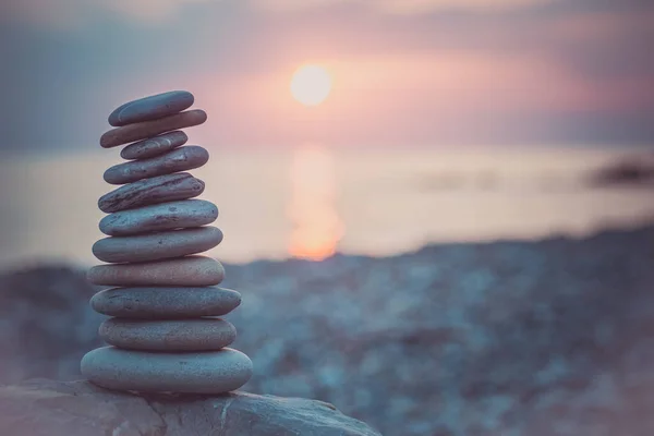 沙子上的石头金字塔象征着禅宗，和谐，平衡。背景为日落时的海洋 — 图库照片