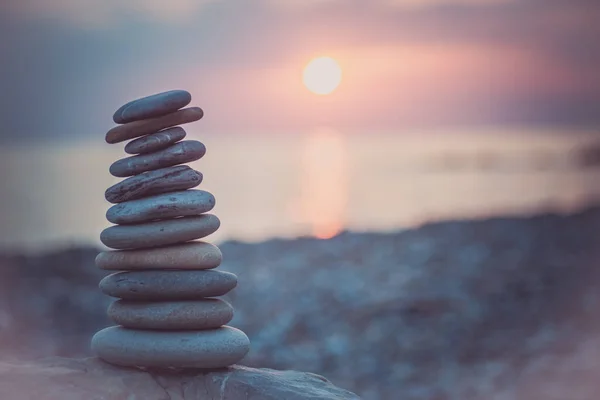 沙子上的石头金字塔象征着禅宗，和谐，平衡。背景为日落时的海洋 — 图库照片