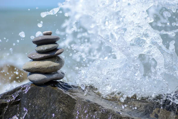 Equilíbrio de pedras zen pirâmide na praia de seixos com uma onda salpicante. Conceito de estabilidade, equilíbrio e harmonia — Fotografia de Stock