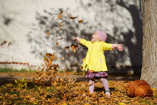 A girl in a yellow dress throws up leaves. Beautiful autumn. Baby and fall foliage.