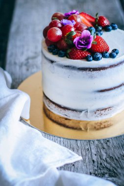 Çilek, yaban mersini, üzüm ve menekşe ahşap arka plan üzerinde çikolatalı kek krem krem ile süslenmiş