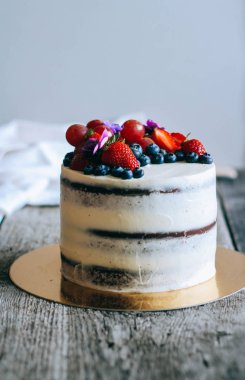 Çilek, yaban mersini, üzüm ve menekşe ahşap arka plan üzerinde çikolatalı kek krem krem ile süslenmiş