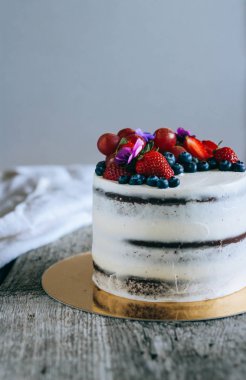 Çilek, yaban mersini, üzüm ve menekşe ahşap arka plan üzerinde çikolatalı kek krem krem ile süslenmiş