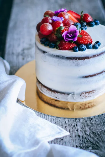 Çilek, yaban mersini, üzüm ve menekşe ahşap arka plan üzerinde çikolatalı kek krem krem ile süslenmiş