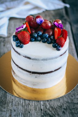 Çilek, yaban mersini, üzüm ve menekşe ahşap arka plan üzerinde çikolatalı kek krem krem ile süslenmiş