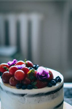 Çilek, yaban mersini, üzüm ve menekşe ahşap arka plan üzerinde çikolatalı kek krem krem ile süslenmiş