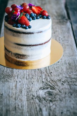Çilek, yaban mersini, üzüm ve menekşe ahşap arka plan üzerinde çikolatalı kek krem krem ile süslenmiş