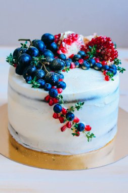 Nar, yaban mersini, üzüm ve menekşe ahşap arka plan üzerinde beyaz Kremalı çikolatalı kek dekore