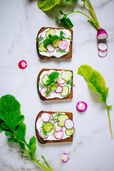 Toast with radish, cucumber and black sesame of dark bread on a light marble background