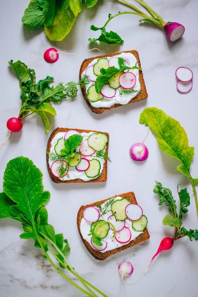 Toast with radish, cucumber and black sesame of dark bread on a light marble background