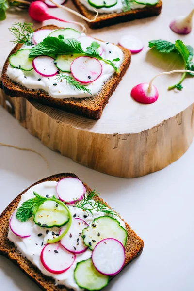 Toast with radish, cucumber and black sesame of dark bread on a light marble background