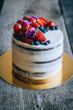 Çilek, yaban mersini, üzüm ve menekşe ahşap arka plan üzerinde çikolatalı kek krem krem ile süslenmiş