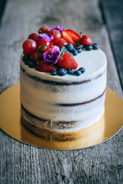 Çilek, yaban mersini, üzüm ve menekşe ahşap arka plan üzerinde çikolatalı kek krem krem ile süslenmiş