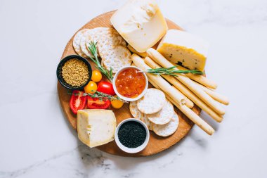Peynir kurulu ile domates, reçel, baget, ekmek sopa ve kraker mermer zemin, üstten görünüm