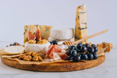 Camembert ve mavi peynir Stilton incir, jamon, bal ve üzüm. Mermer zemin üzerine peynir tabağı