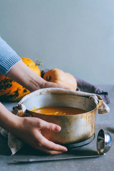 Casserole of hot pumpkin soup in the hands of a girl on a gray background, bright pumpkin