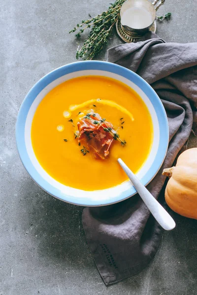 Bir tabak krem, jambon ve kekik, gri bir arka planda üstten görünüm ile kabak çorbası
