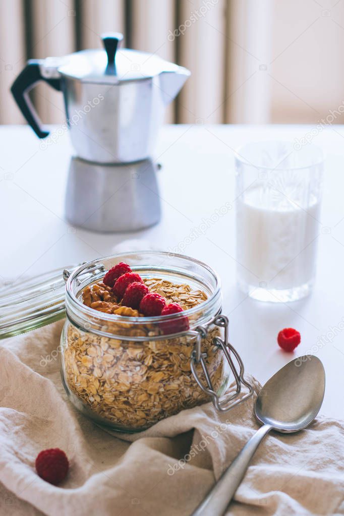  Morning breakfast, oatmeal with red raspberries, walnuts in a glass jar a coffee pot glas of milk