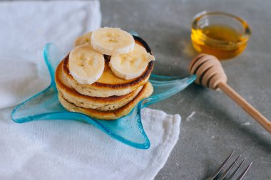 Tatlı ev yapımı yığın krep muz ve gri arka plan üzerinde yıldız tabakta bal ile