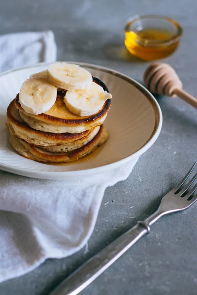 Sweet homemade stack of pancakes with banana and honey on gray background