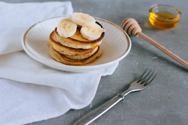 Sweet homemade stack of pancakes with banana and honey on gray background