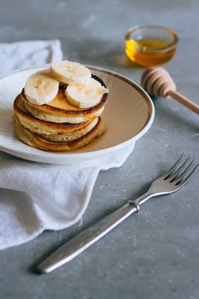 Sweet homemade stack of pancakes with banana and honey on gray background