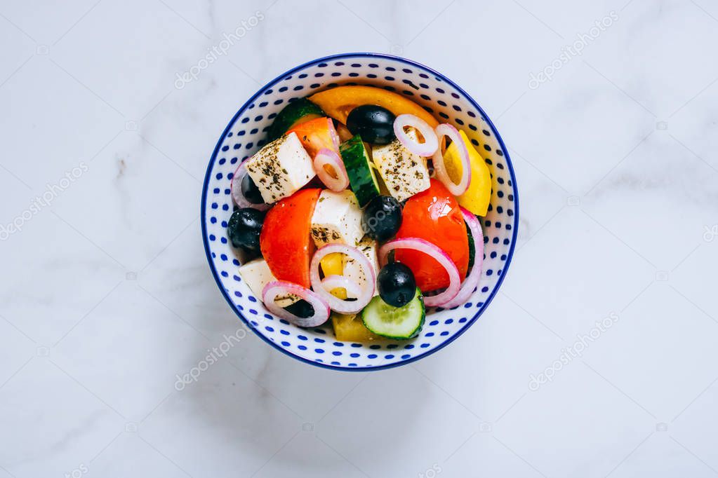 Top view greek salad of fresh cucumber, tomato, sweet pepper, red onion, feta cheese and olives with olive oil on marble.