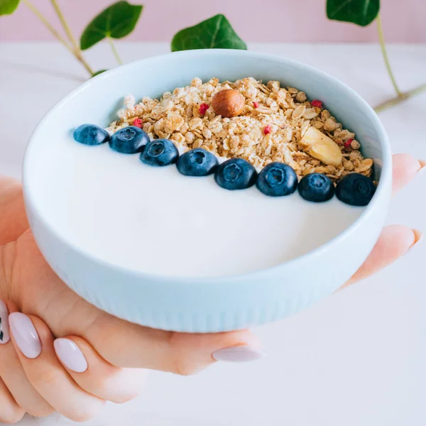 Healthy breakfast bowl with muesli and yogurt in woman hands on pink and marble background. Clean eating, vegetarian, vegan, alkiline diet food concept — Stock Photo, Image