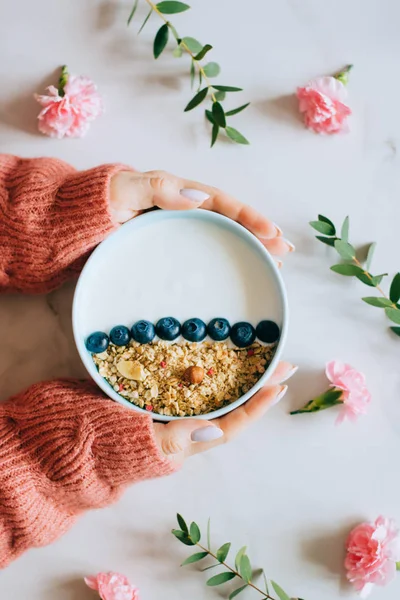 Woman in coral woolen sweater eating breakfast bowl with muesli and yogurt, berries and hazelnuts. Clean eating, vegetarian, vegan, alkiline diet food concept — Stock Photo, Image