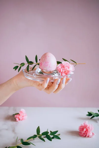 The girl is holding a pink easter egg on a stand, pink and marble background, minimalism, flowers