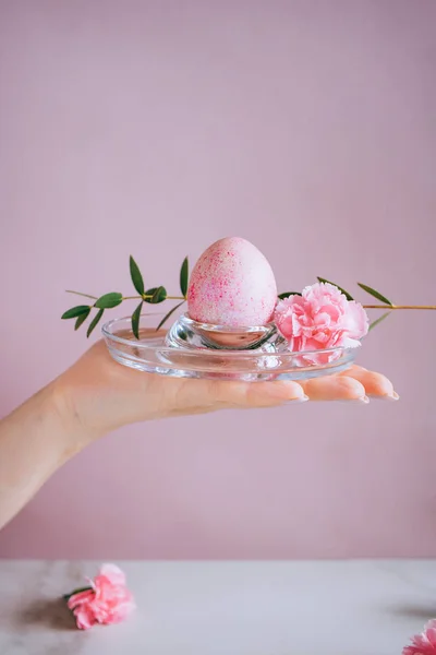 The girl is holding a pink easter egg on a stand, pink and marble background, minimalism, flowers