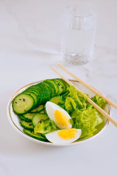 Здорова миска, салат з огірками з яйцями та склянкою води на мармуровому фоні — стокове фото