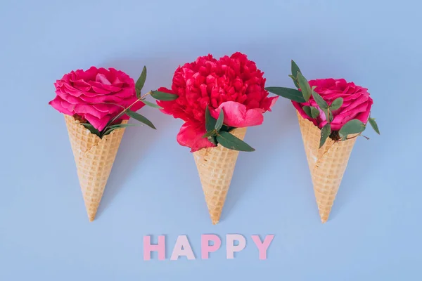 Ice Cream Cones with pink peony and roses on blue background, flat lay. Happy text — Stock Photo, Image