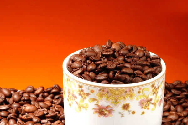 A cup of coffee with fried beans on an orange background. Top for text.