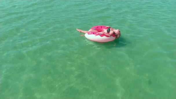 性感的年轻女孩在太阳镜女孩在粉红色的橡胶甜甜圈环上摆姿势与波浪 — 图库视频影像