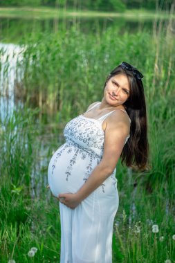 Bir gölet yakınındaki beyaz giysili bir hamile kadına