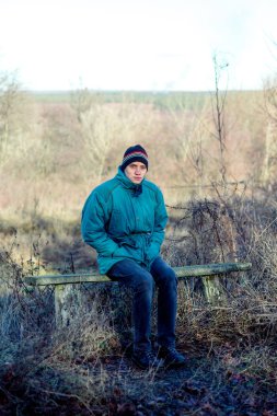 Genç bir adam sonbahar zamanında kırsal kesimde eski bir bankta oturur