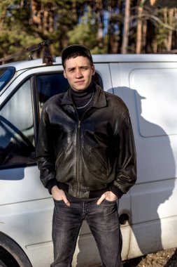 Genç bir adam bir siyah deri ceketli suç görünüm eski bir beyaz van duruyor.