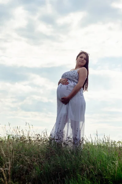 Bulutlu Gökyüzü Karşı Bir Çayırda Beyaz Giysili Bir Hamile Kadına — Stok fotoğraf