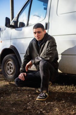 Genç bir adam bir siyah deri ceketli suç görünüm eski bir beyaz van duruyor