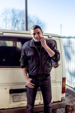 Genç bir adam bir siyah deri ceketli suç görünüm eski bir beyaz van duruyor.