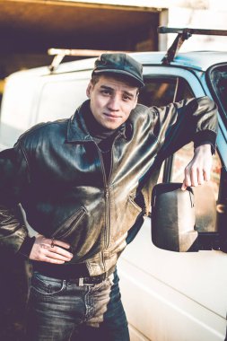 Genç bir adam bir siyah deri ceketli suç görünüm eski bir beyaz van duruyor.
