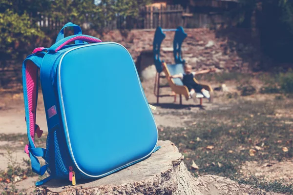 stock image Back to school concept. A school backpack in the foreground and a junior schoolgirl on the playground in the background. Accent photos on a school backpack.