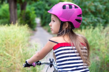 Yaz aylarında bir bisiklet yakınındaki pembe bir kask içinde küçük şirin kız